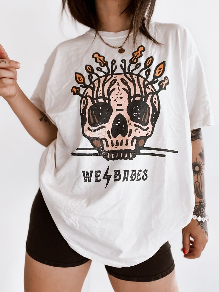 These tees are printed on super soft Comfort Colors, providing a relaxed unisex fit with a worn-in look and feel. This collection offers our most expanded size range from S-3X.Looking for these tees to fit oversized? Size up 1-2 sizes.Model has sized up to an 2X for an oversized fit.• 100% ring-spun cotton• Garment-dyed• Relaxed fitThis product is made especially for you as soon as you place an order, please see the banner on the top of our site for current turnaround times. Making products on d Edgy Skull Graphic Print T-shirt, Edgy White Skull Print Top, Edgy White Top With Skull Print, White Cotton T-shirt With Skull Print, Skull Graphic Tee With Text Print, Edgy Skull Print Relaxed Fit T-shirt, Halloween Graphic T-shirt With Relaxed Fit, Halloween Graphic T-shirt Relaxed Fit, Unisex Cotton T-shirt With Skull Print