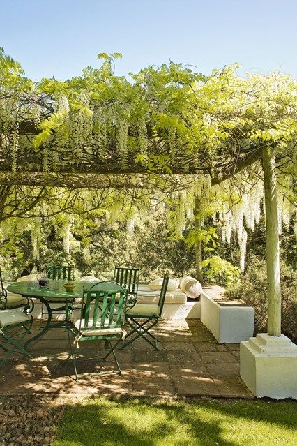 a table and chairs under an arbor with moss growing on the branches overhanging it