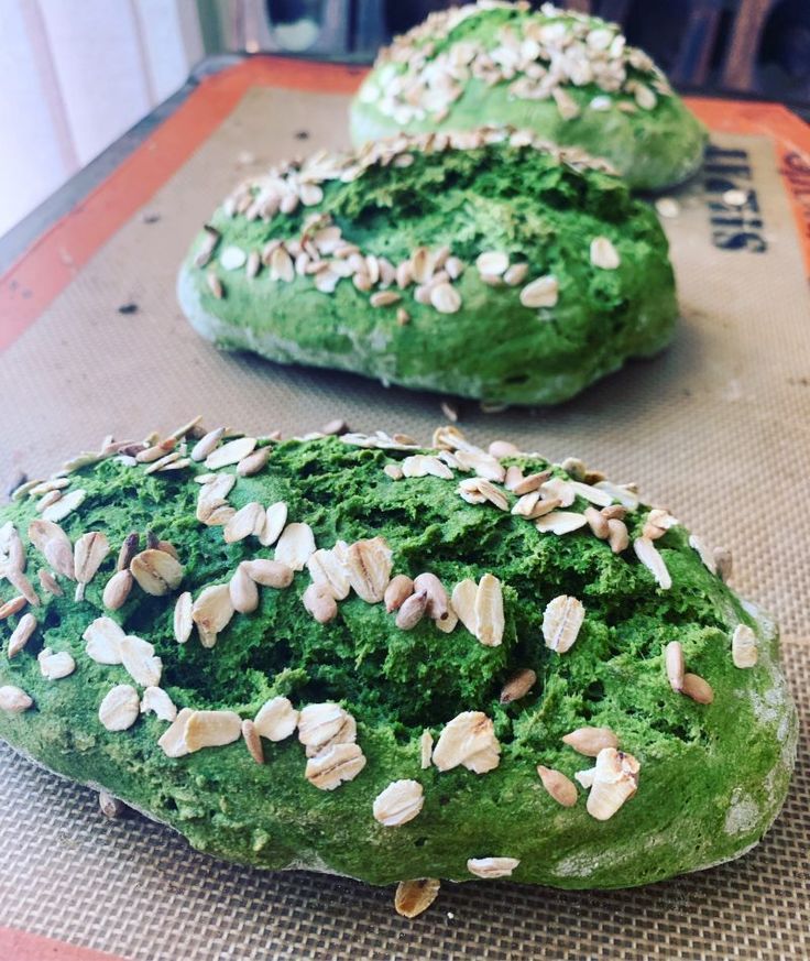 two doughnuts covered in green and white frosting with nuts on top, sitting on a baking sheet