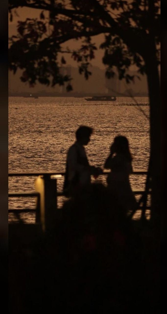 two people sitting next to each other on a bench near the water at night time