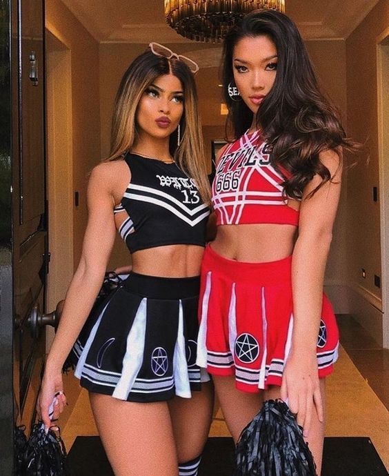 two beautiful young women standing next to each other in cheerleader outfits and holding umbrellas