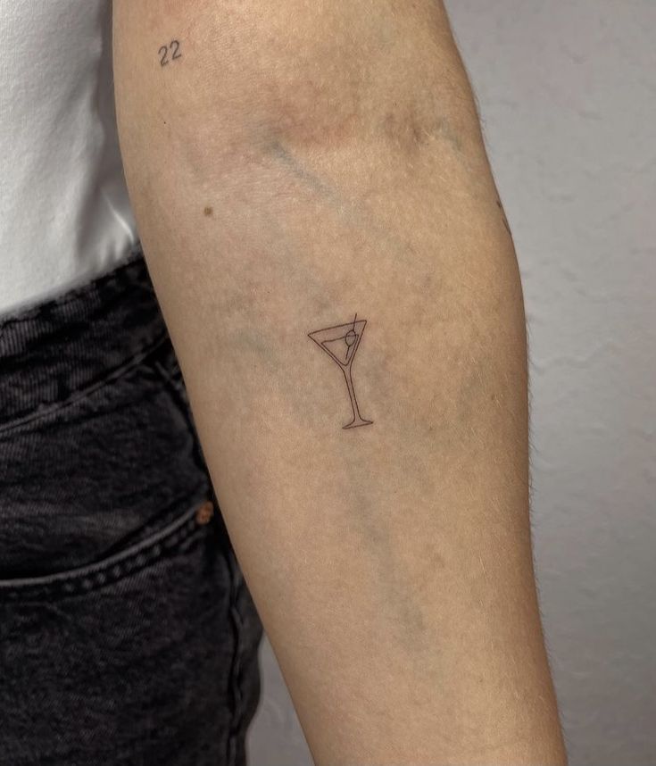 a woman's arm with a small martini tattoo on the left side of her arm