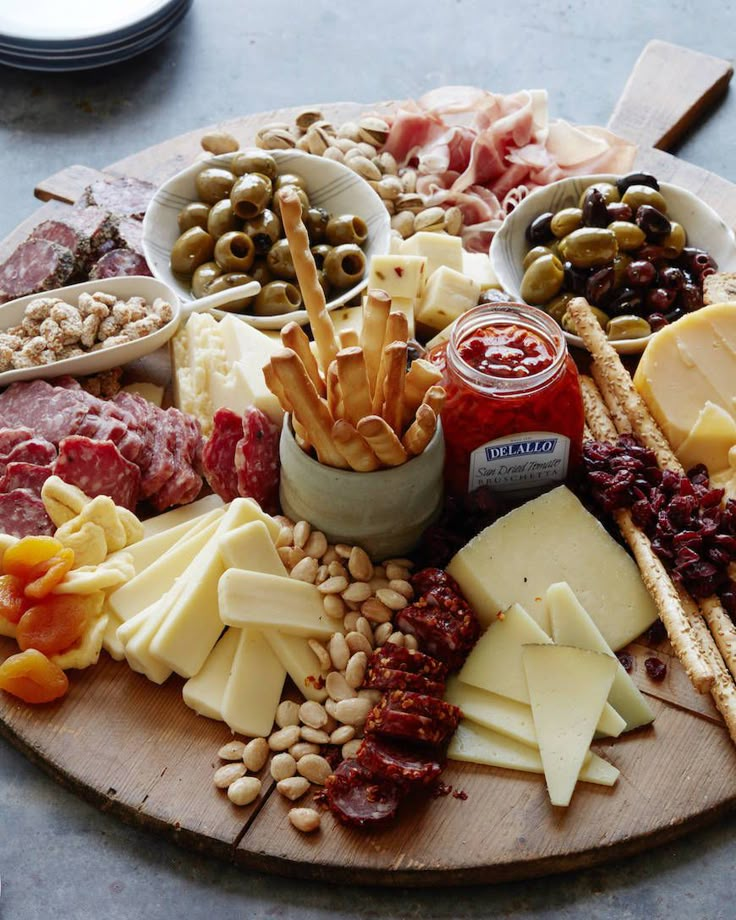 an assortment of cheeses, meats and nuts on a wooden platter with olives