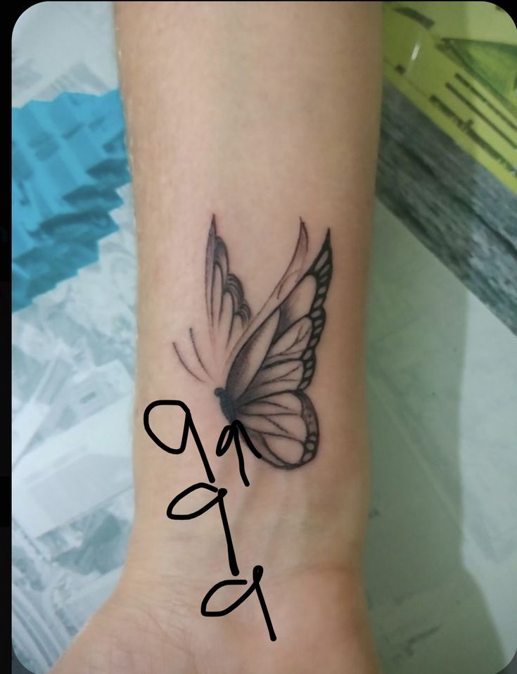 a small butterfly tattoo on the wrist is shown in black and grey ink, with white wings