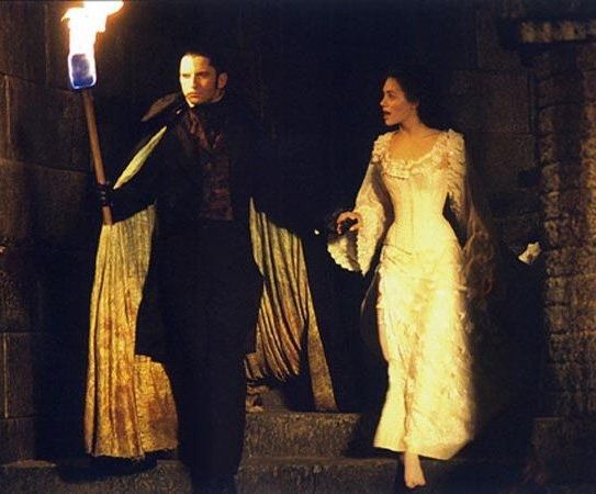 a man and woman dressed in period costumes walking down the stairs with torches on their heads