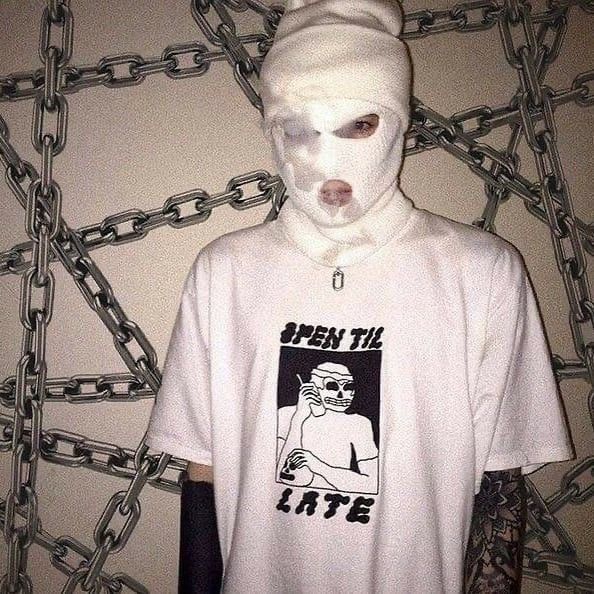 a person wearing a white mask and t - shirt with chains on the wall behind them