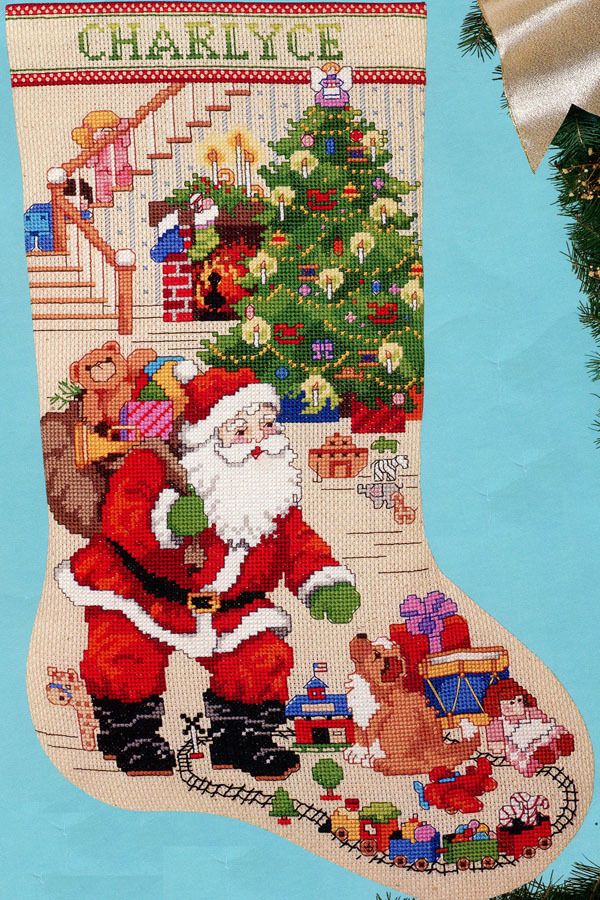 a cross stitch christmas stocking with santa and his stockings hanging from the tree, on a blue background