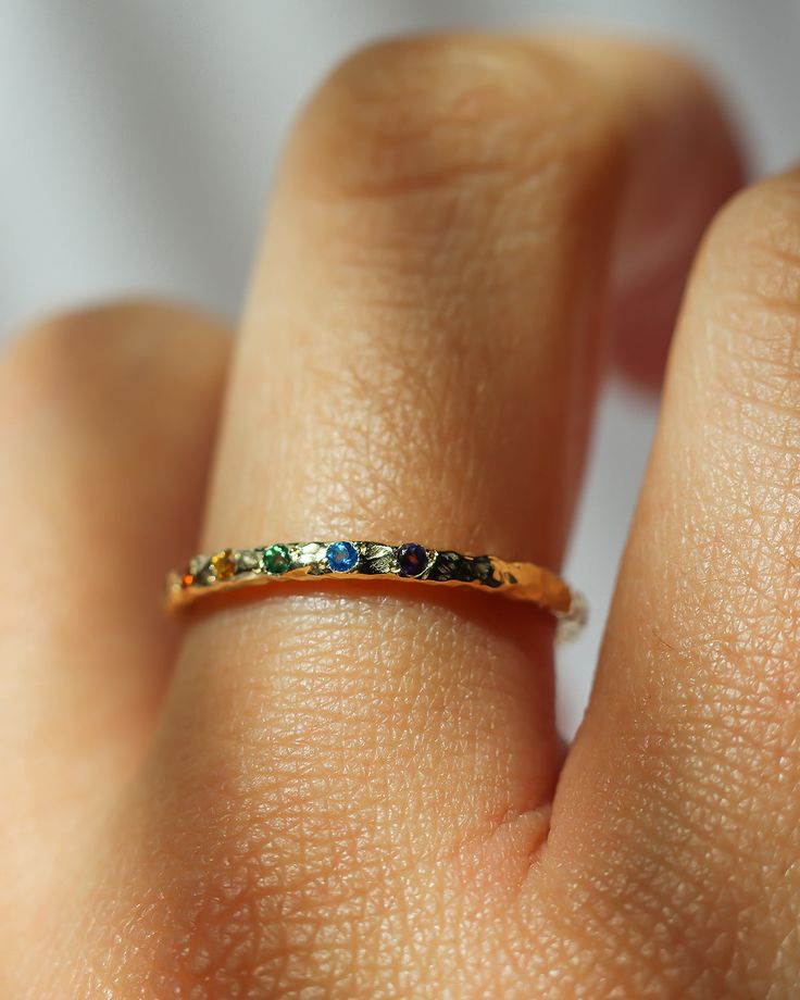 a person's hand with a gold ring on their finger and colorful stones in the middle