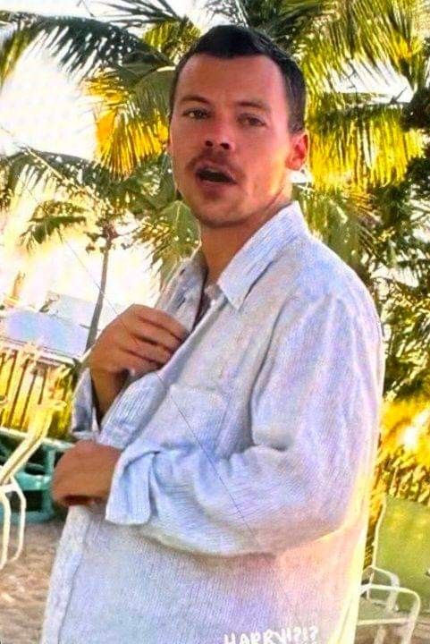 a man standing in front of a palm tree with his tie around his neck and looking at the camera