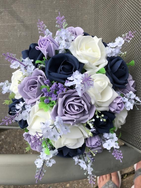 a bridal bouquet with purple and white flowers on the back of a chair in front of someone's feet