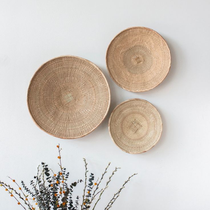 three woven baskets hanging on the wall next to a vase with dried flowers in it