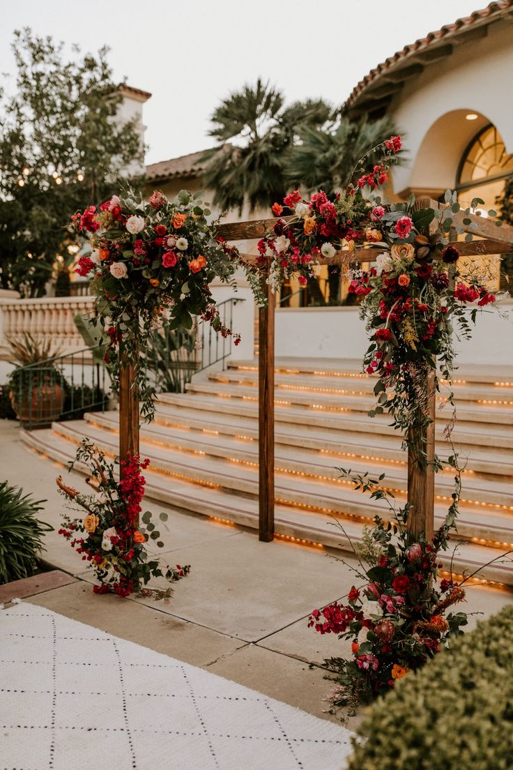 an outdoor ceremony setup with red flowers and greenery on the side of the aisle