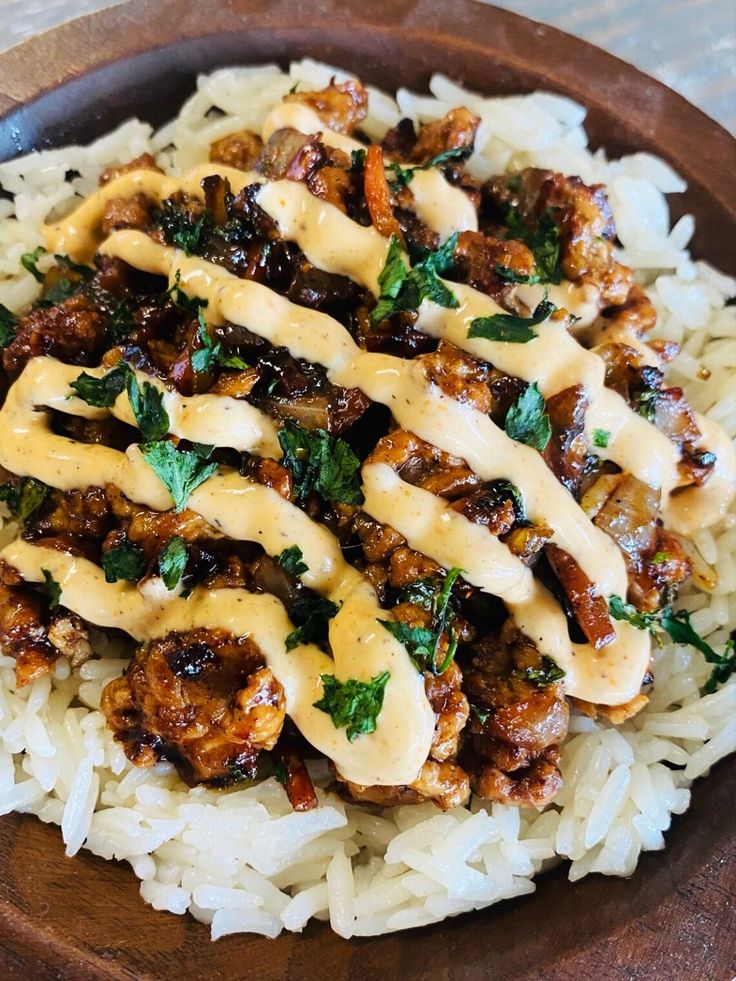 a wooden bowl filled with rice and meat covered in gravy on top of it