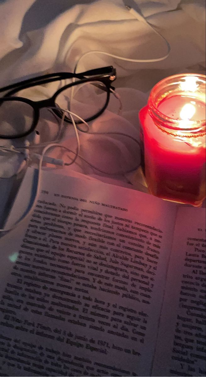 an open book with glasses on it next to a lit candle