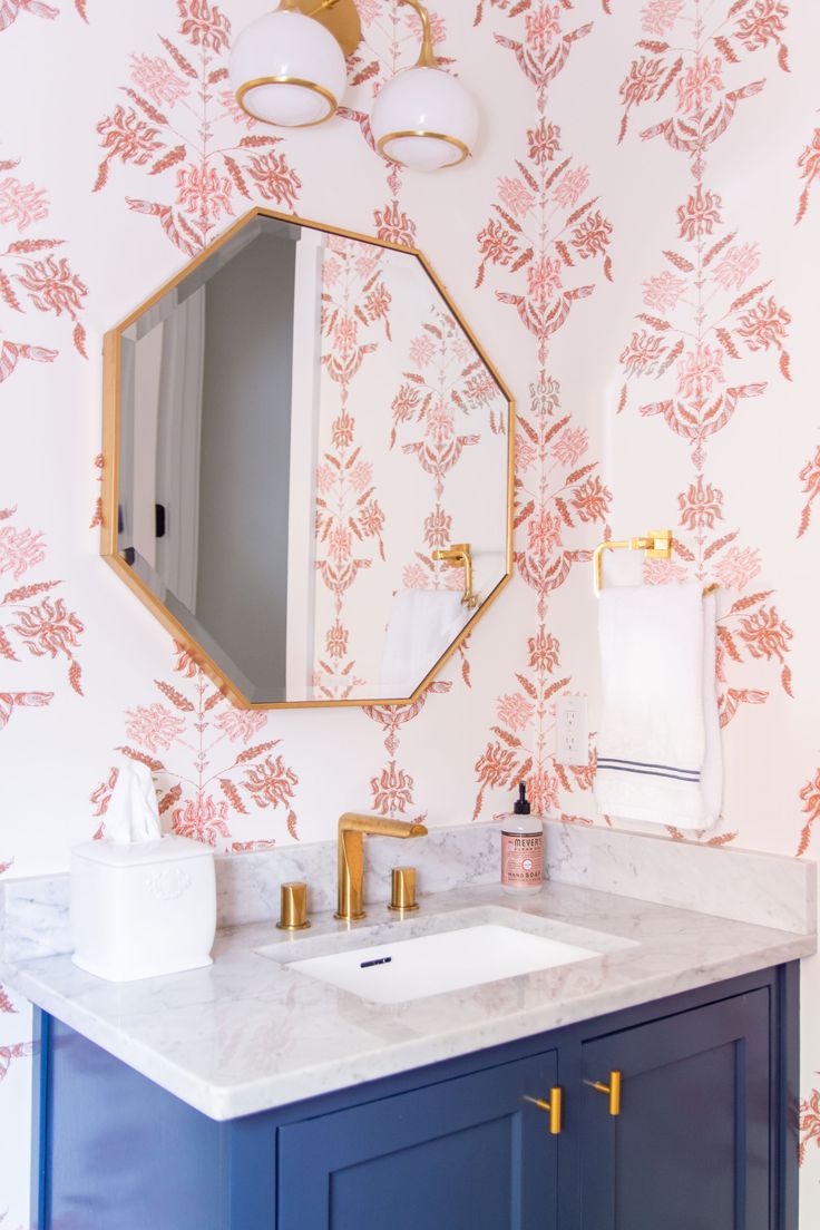 a bathroom with pink and white wallpaper, gold fixtures and blue vanity