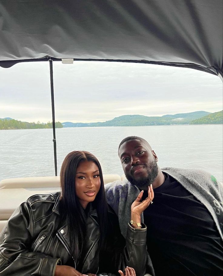 a man and woman sitting on a boat in front of the water, posing for a photo