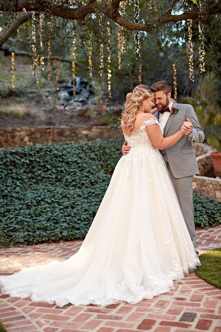 a bride and groom pose for a photo in front of a tree with lights hanging from it