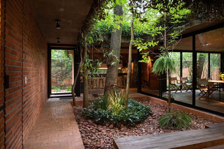 the inside of a house with trees and plants on the outside wall, surrounded by brick walkways