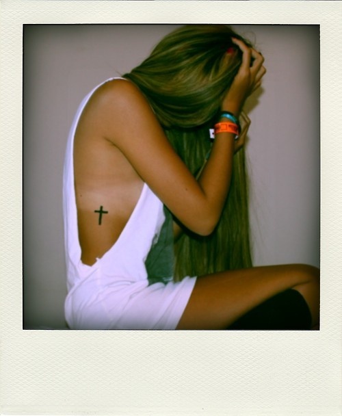 a woman with long hair sitting on the floor wearing bracelets and a cross tattoo