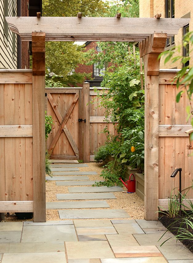 an open wooden gate in the middle of a small garden with plants and flowers on either side