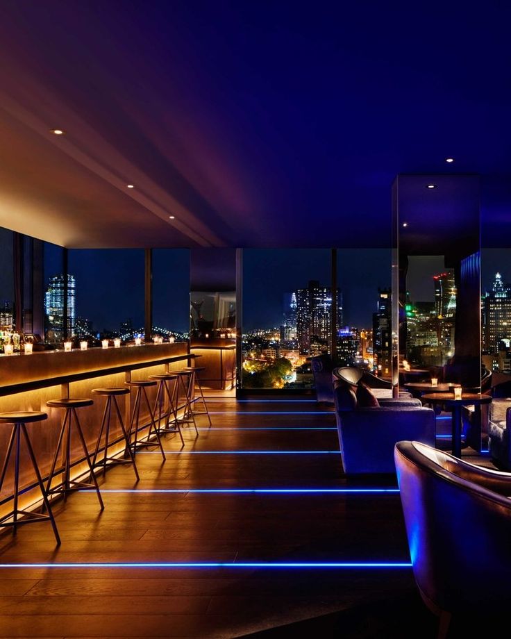 the bar is lit up at night with blue lights in the room and tall buildings behind it