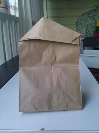 a brown paper bag sitting on top of a white table next to a chair and window