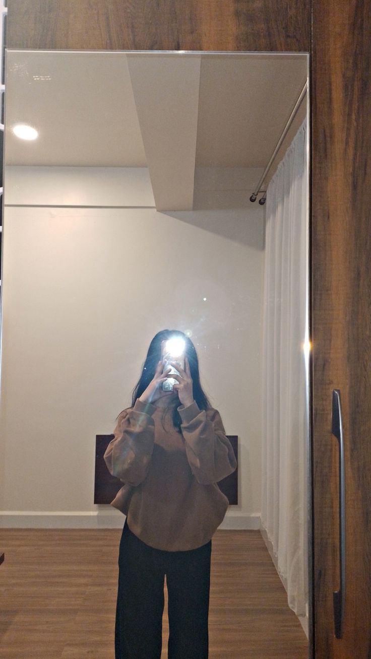 a woman is taking a photo in the mirror with her cell phone while standing on a wooden floor