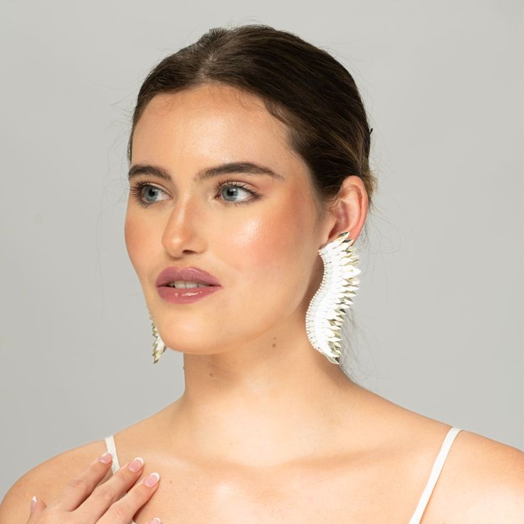 Bring the elegance of white gold into your ensembles in a fresh new way when you don the White Gold Small Wing Earrings at your next dinner party or wedding. Handmade with care, they are a statement piece that will match all your looks. The earrings boast layers of white and gold-toned beads arranged atop one another in a wing-like shape, creating the silhouette of these angel wing earrings. Size: Length: 3.5''/ Width: 1'' Elegant White Linear Pierced Earrings, Chic Silver Linear Earrings For Wedding, Modern Dangle Bridal Earrings For Party, Elegant White Clip-on Earrings, Modern White Linear Earrings For Formal Occasions, Chic Silver Chandelier Earrings For Wedding, Modern Chandelier Drop Earrings For Wedding, Evening White Gold Pierced Bridal Earrings, Modern Bridal Earrings For Parties