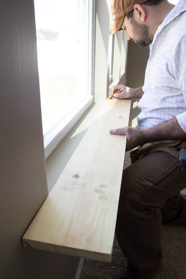 a man working on a window sill in front of a window with wood planks