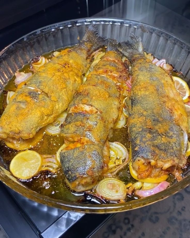 some fish are cooking in a pan with lemons and onions on the stove top