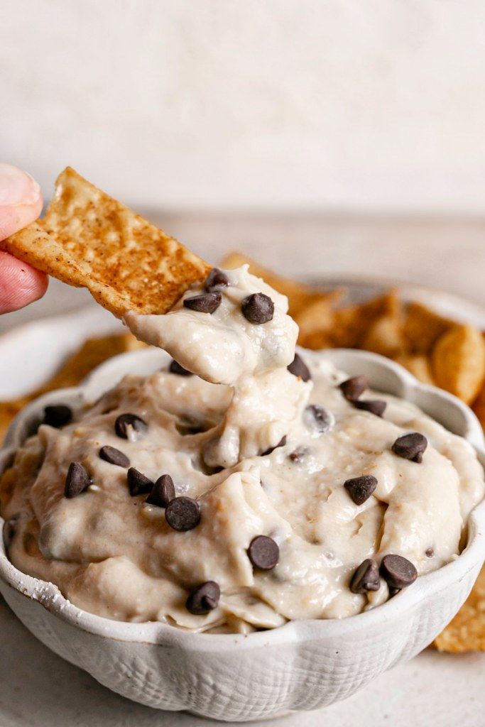 a hand holding a cracker over a bowl of ice cream with chocolate chips on the side