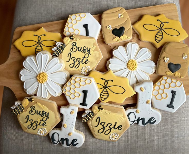 decorated cookies are arranged in the shape of honeybees and daisies on a cutting board