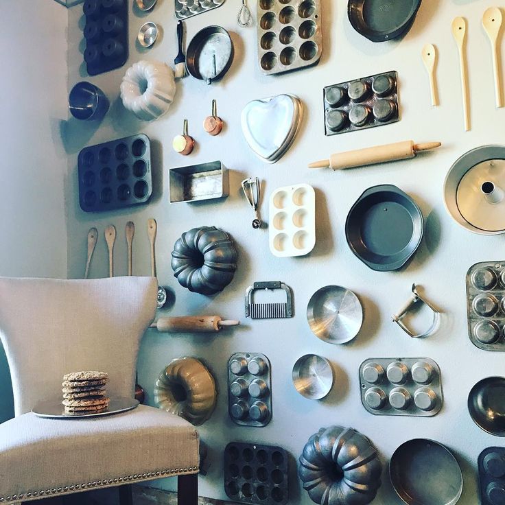 an assortment of kitchen utensils and pans on a wall above a chair