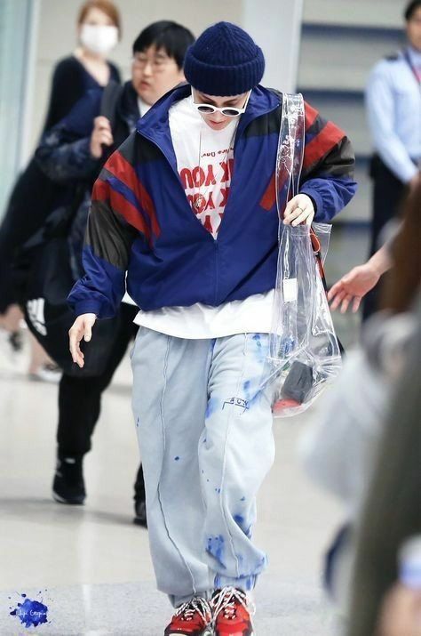 a man walking through an airport carrying a plastic bag with blue paint all over it