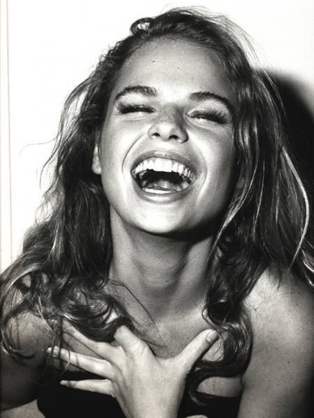 a black and white photo of a woman laughing with her hands on her chest,