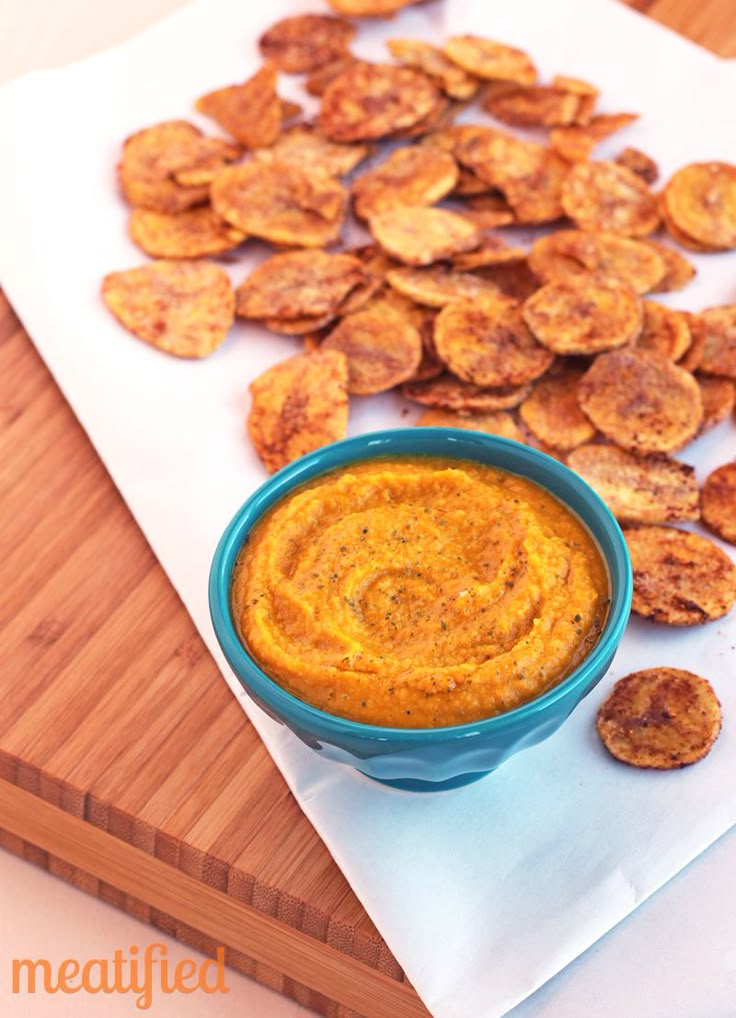 a blue bowl filled with dip next to some fried potato chips on a cutting board