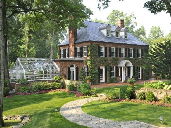 a large brick house surrounded by lush green grass and trees, with a walkway leading to the front door