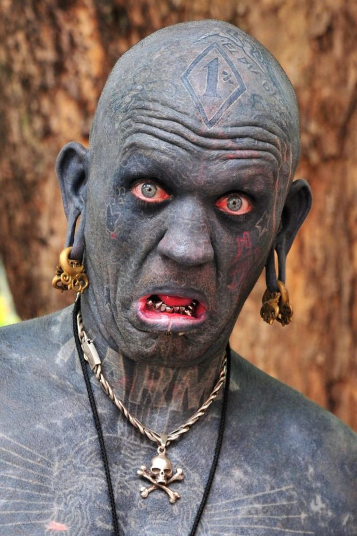 a man with tattoos and piercings on his face standing in front of a tree