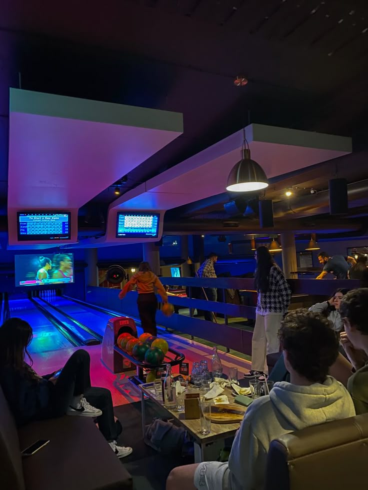 several people are bowling in a bowling alley at night time, with neon lights on the ceiling