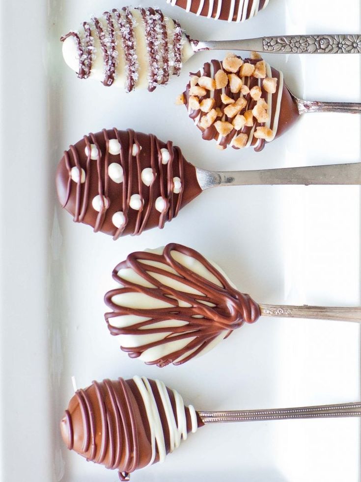 four chocolate covered desserts are lined up on a white tray with utensils