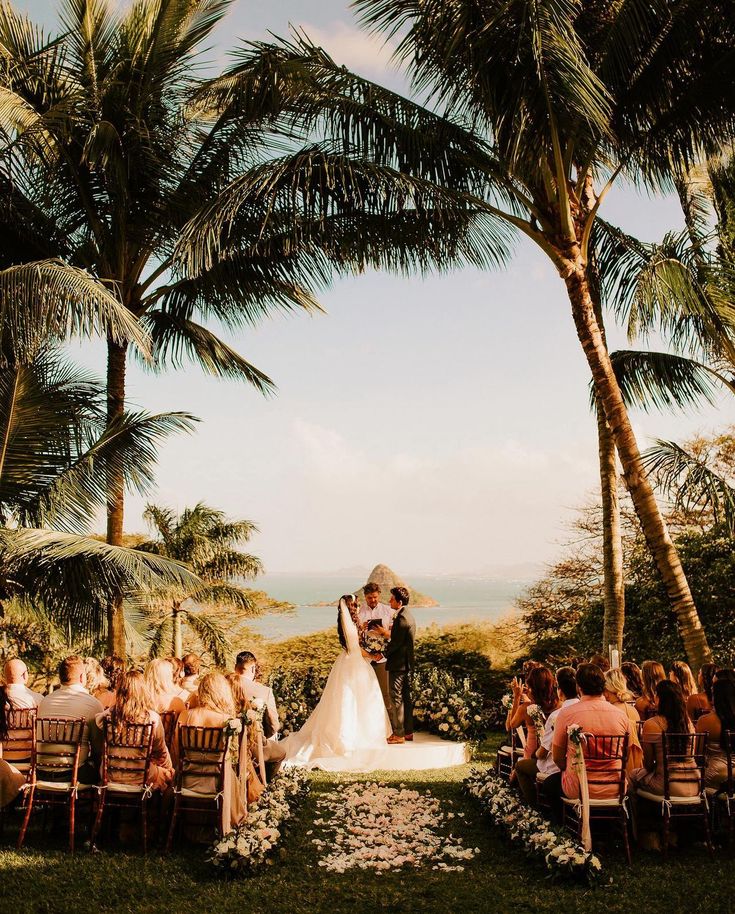 a bride and groom standing in front of palm trees at their outdoor wedding ceremony with the ocean in the background