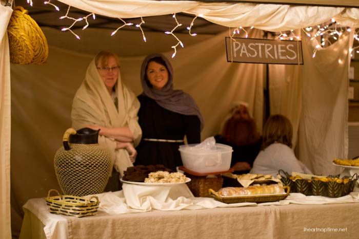 two women standing in front of a table with food on it and lights strung from the ceiling