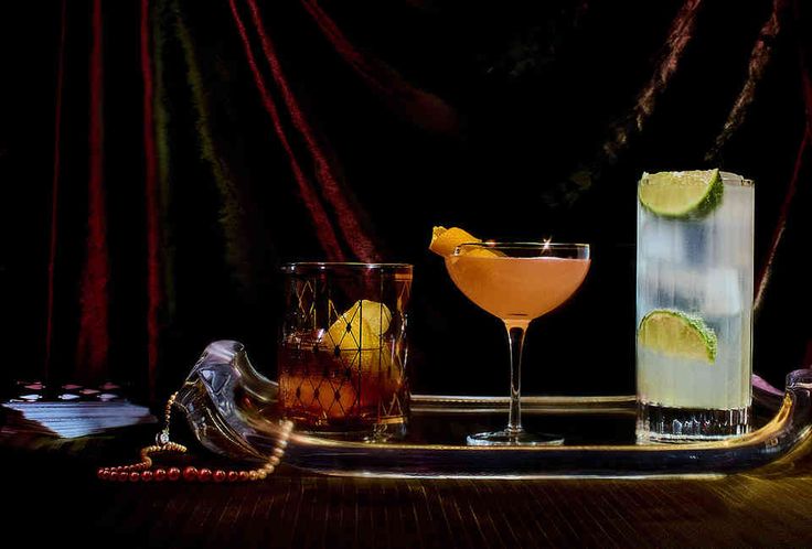 three different types of cocktails on a tray with red curtains in the back ground