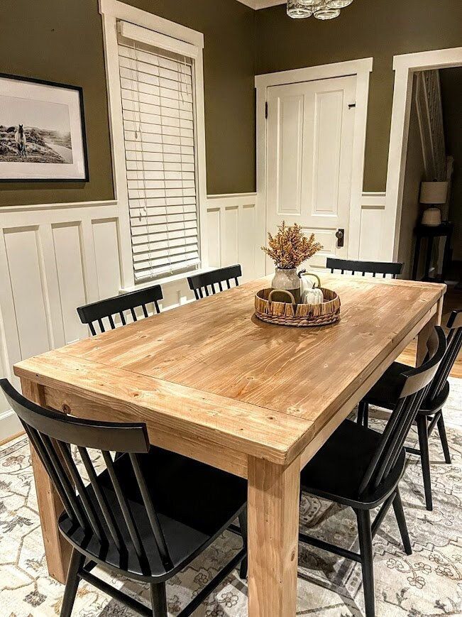 a dining room table with black chairs and a basket on top of it in front of a white paneled door