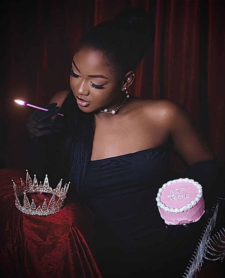 a woman in a black dress holding a pink cake with a lit candle on it