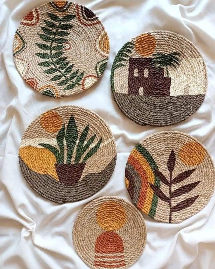 four woven coasters with designs on them sitting on a white cloth covered bed sheet