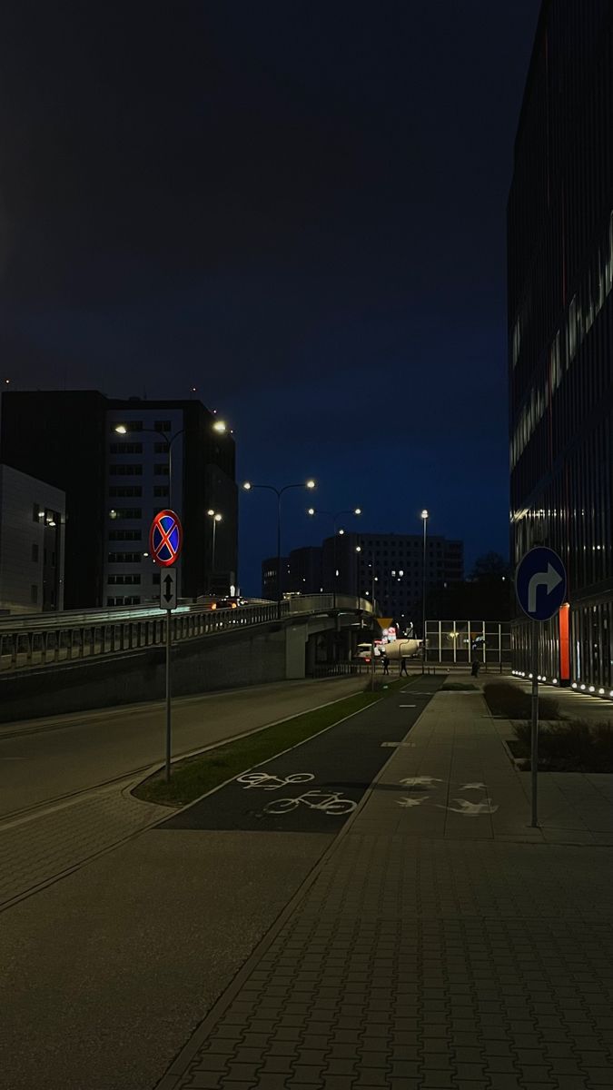 an empty city street at night with no cars or people on the road and buildings in the background