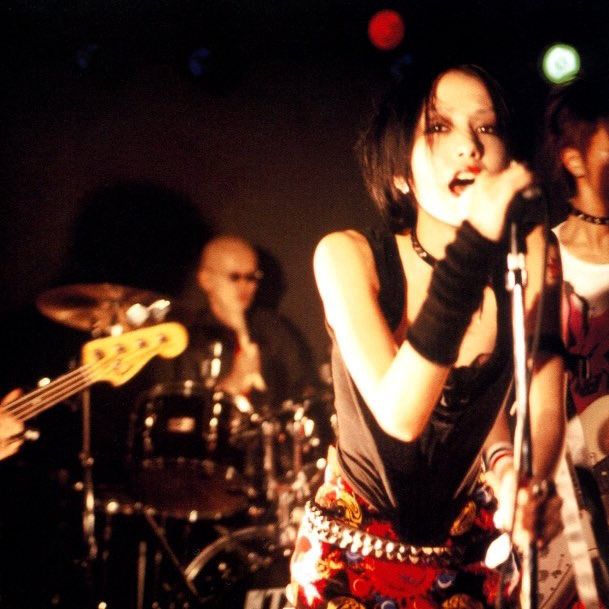 a woman singing into a microphone while standing in front of two other people on stage