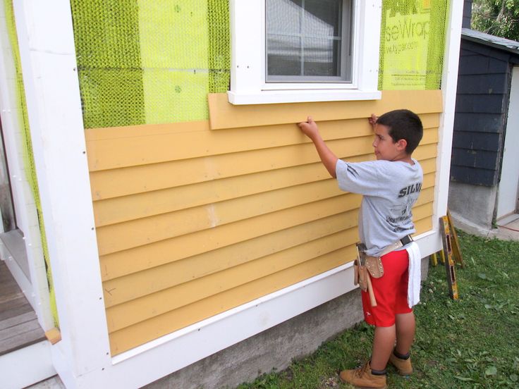 a little boy that is standing in front of a house painting the side of a house