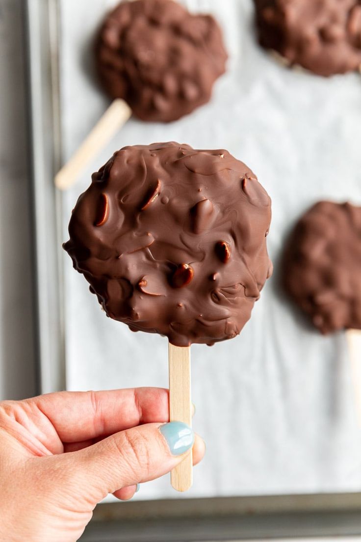 a hand holding a chocolate covered lollipop on a stick